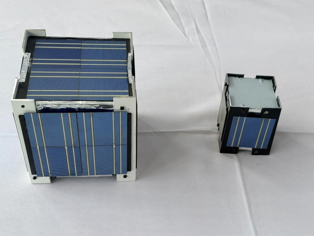Two of the first NMD satellites side by side on a white cloth, each covered with blue solar cells